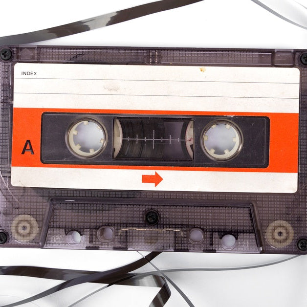 A clear cassette tape with an orange label lying among loose black tape strands and loops on a white surface.
